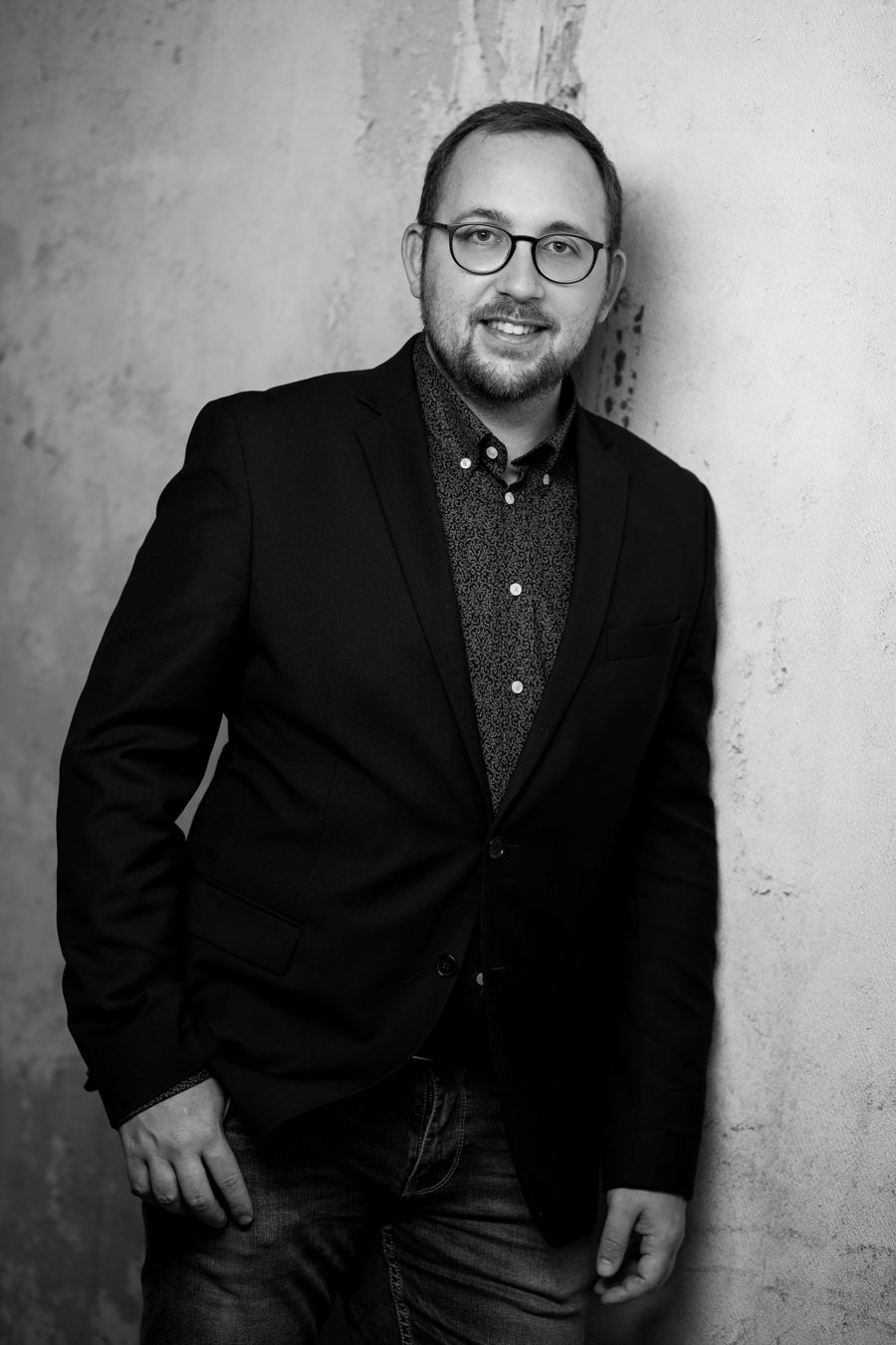 Florian Pfeifer, lehnt im Sakko an einer Betonwand